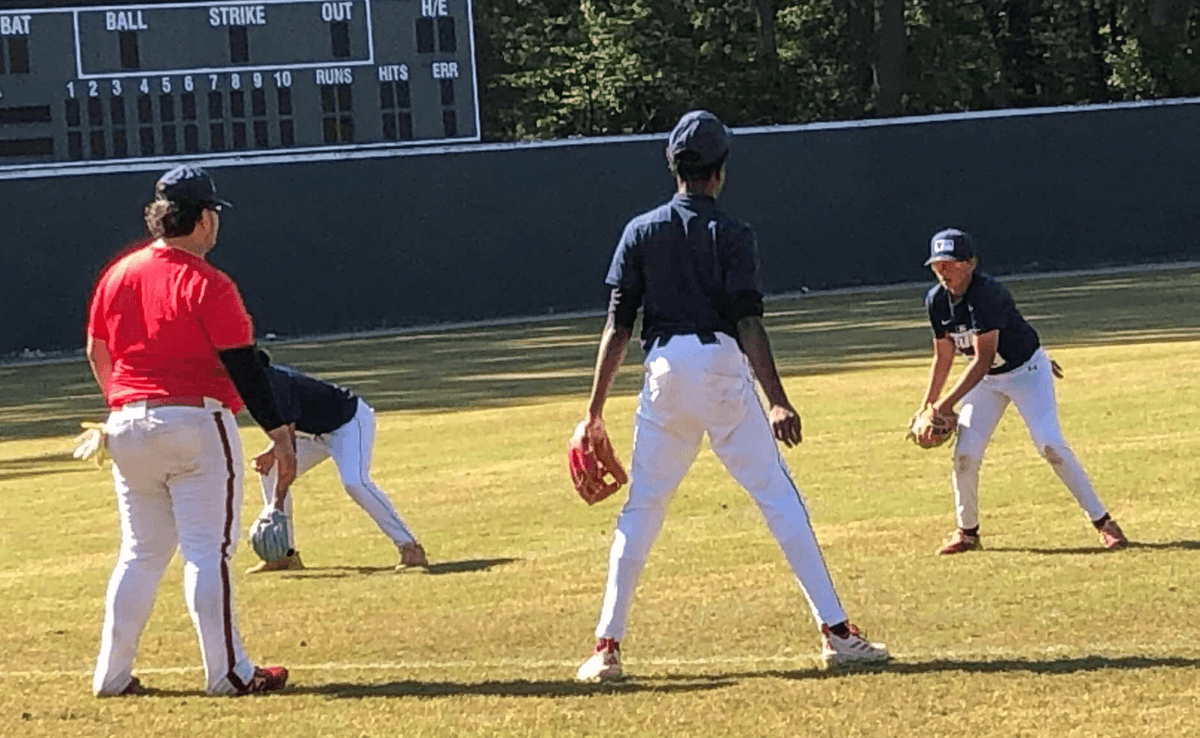 A coach in a red jersey instructs young infielders in fielding stance during the Palmetto Baseball Prospects clinic at Duncan Park Stadium