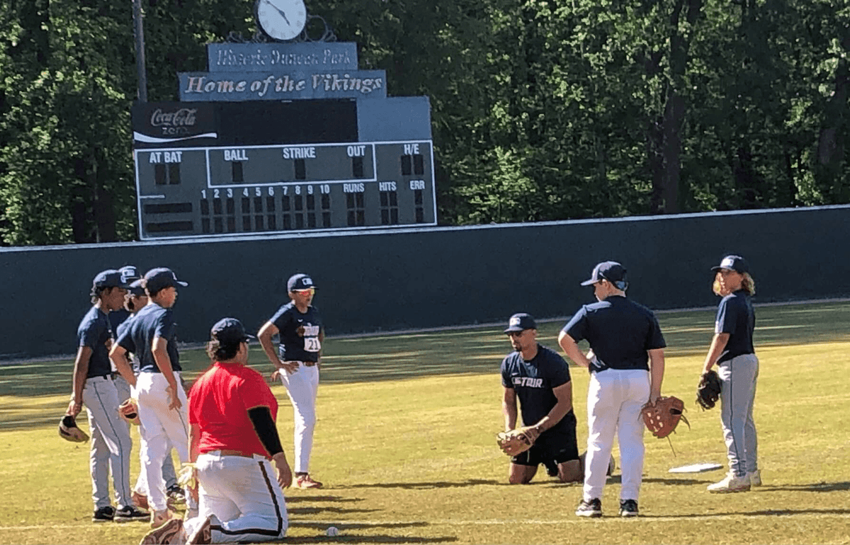 Young baseball players in navy jerseys gather on the field at Historic Duncan Park Stadium during the MLB and Palmetto Baseball Prospects youth clinic, with the "Home of the Vikings" scoreboard visible in the background