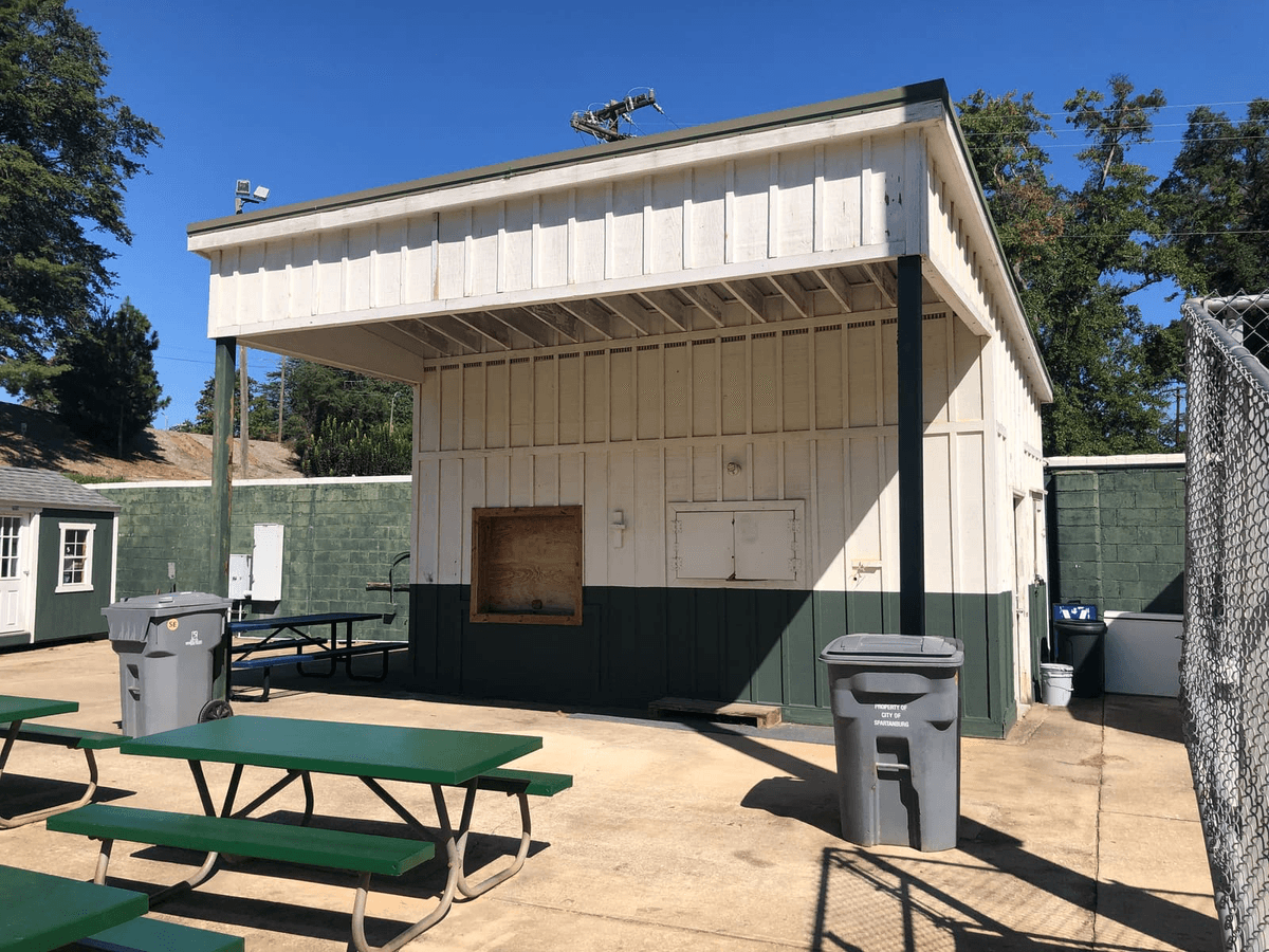 The current “concessions stand” between the lower entrance gate and the bleachers and restrooms is barely adequate for snacks and cold drinks. It would be possible to use a hotplate and/or crock pot to heat chili and hot dogs, but there is no way to really cook anything. And while there are tables and benches to sit at, these are unshaded and open to exposure during bad weather.